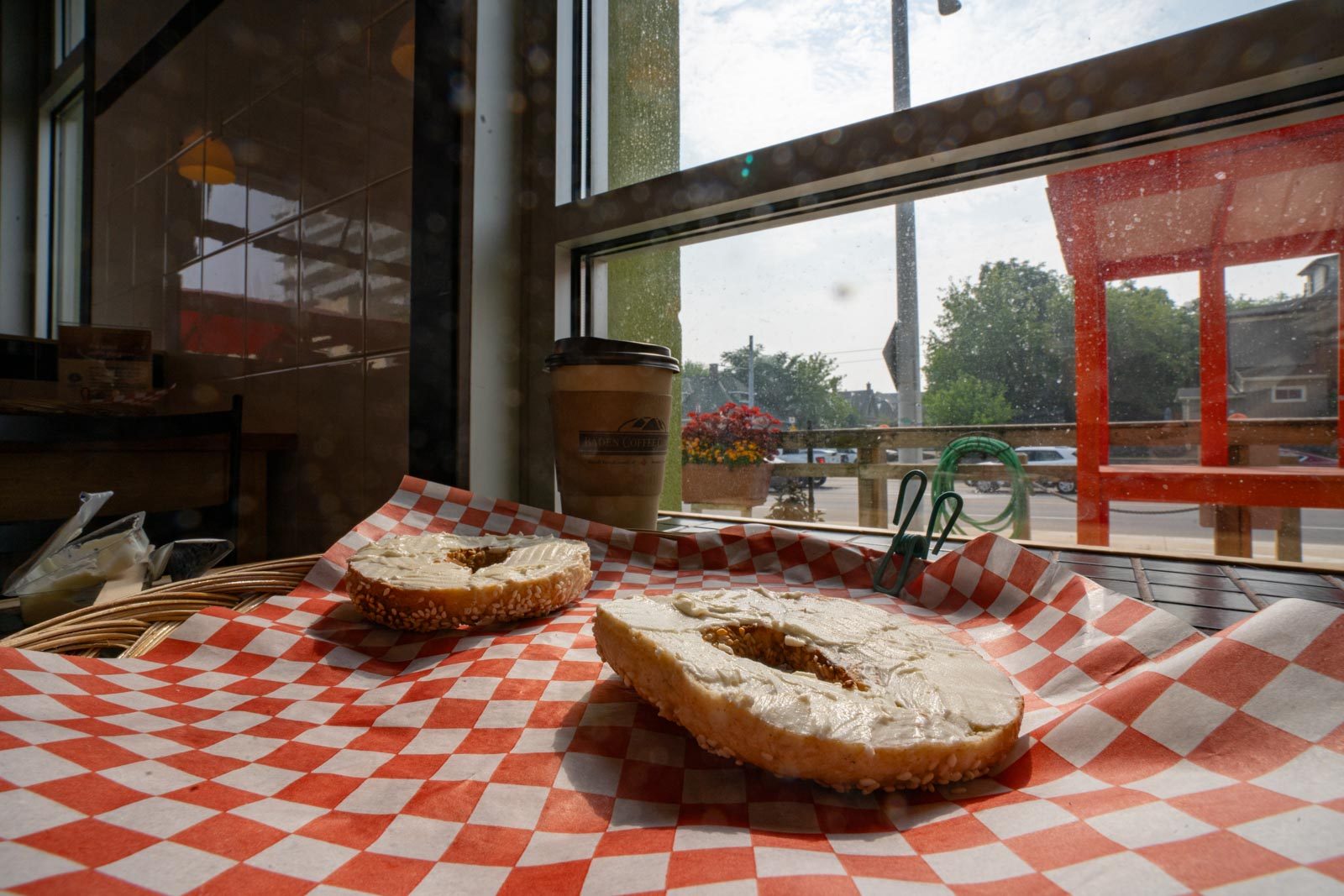 A sliced bagel spread with cream cheese on red checked paper